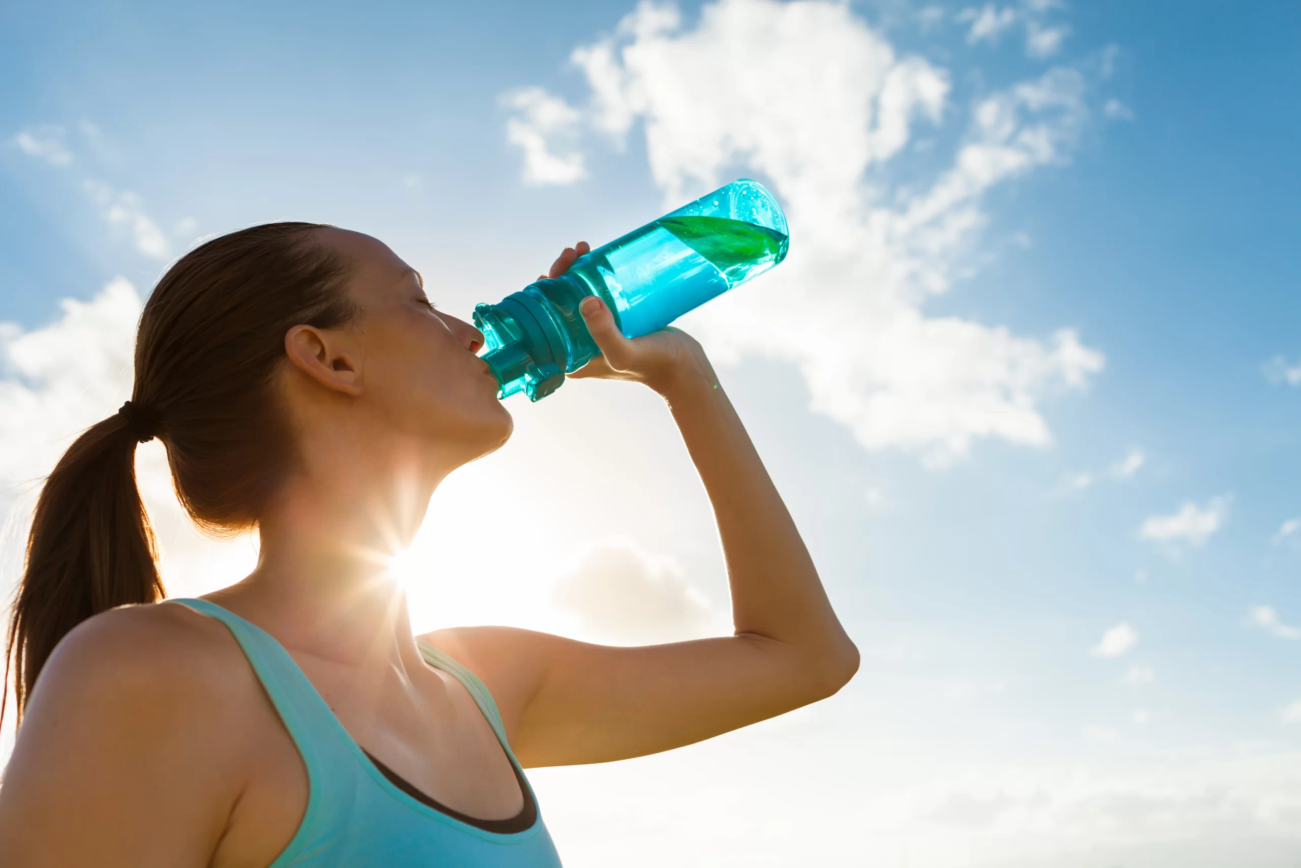 Woman drinking bottle of water to stay hydrated and prevent muscle spasms